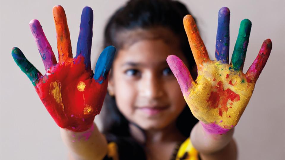 A young girl with rainbow paint on the palms of her hands