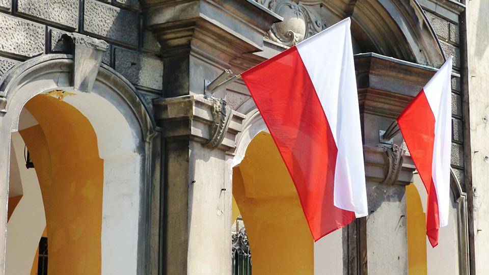 Two red and white Polish flags hang from a building