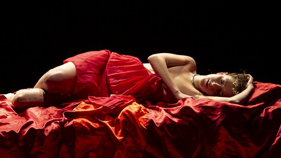 A performer on a red drape, with a red sheet over her