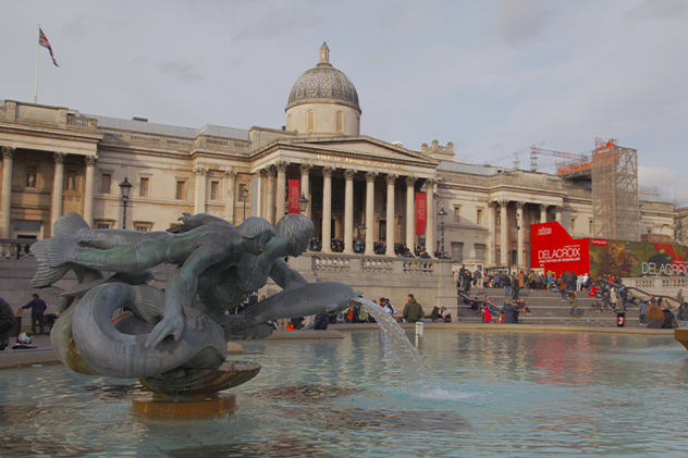 Exterior of National Gallery in Trafalgar Square with fountain in foreground.