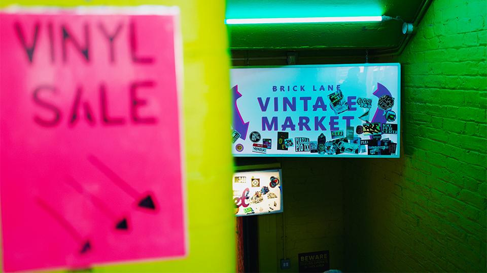 A sign lit in green that reads 'Brick Lane Vintage Market'