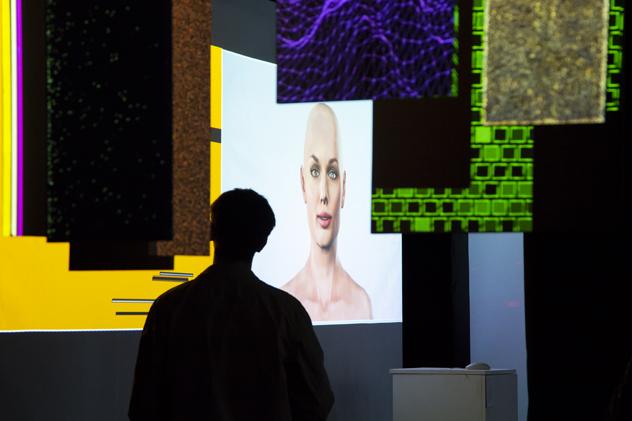 A silhouette of a visitor at the Goldsmiths undergraduate degree show, looking at a screen featuring a computer-generated human face