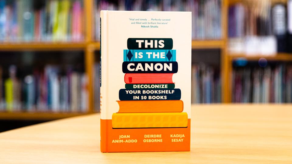 Image shows the book This is the Canon standing upright on a table in a library. The book cover has pictures of book spines on it.