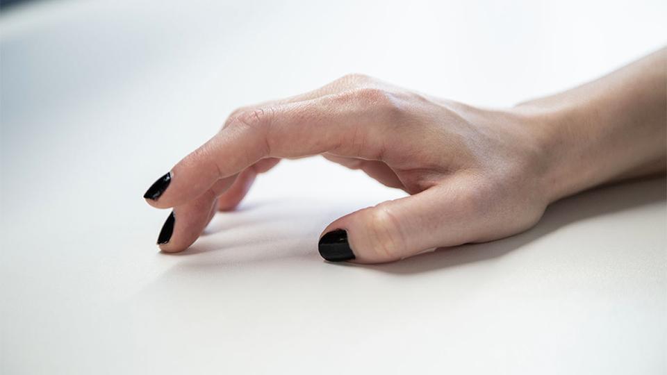 Image shows a female hand with black nail varnish tapping on a white table