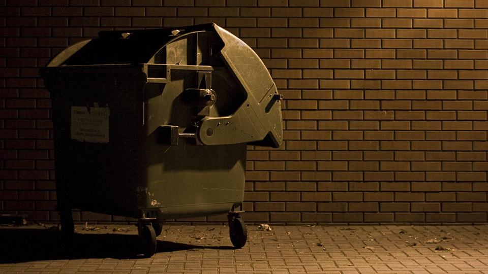 Image shows a commercial rubbish bin in a street at night