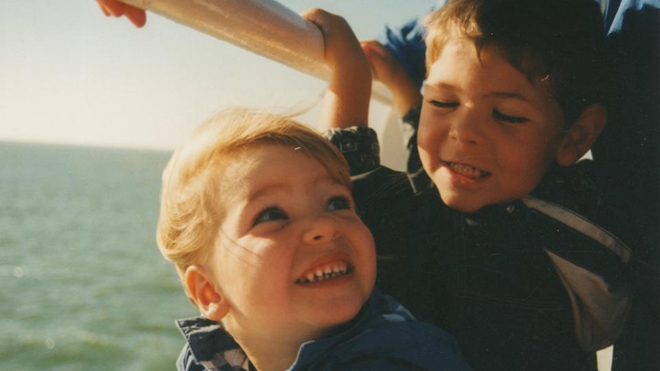 Image shows a young boy and girl smiling and clinging to the railing on the side of a boat