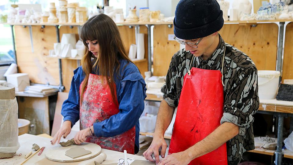 Two students in aprons creating the prize from clay 