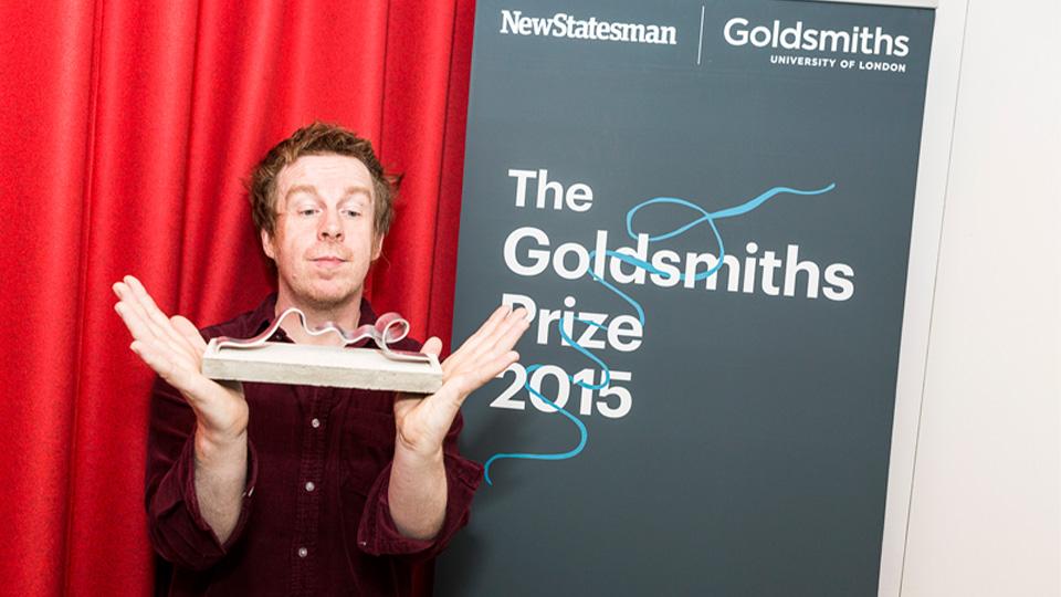 A photograph of Kevin Barry holding the Goldsmiths Prize at the award ceremony in 2015