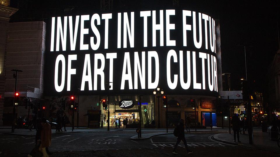 Image shows a large electronic billboard displaying the words INVEST IN THE FUTURE OF ART AND CULTURE