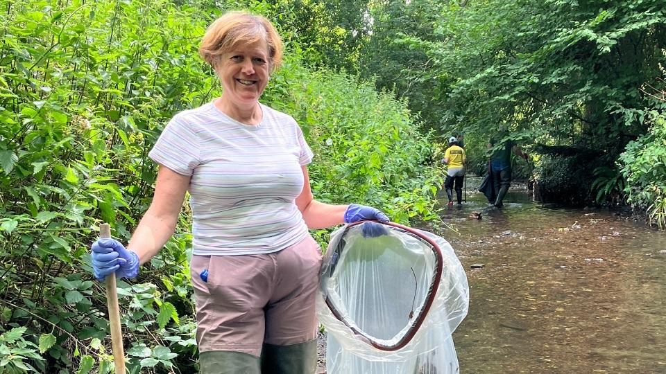Marian Perez-Velazquez standing in a river, holding clean-up equipment