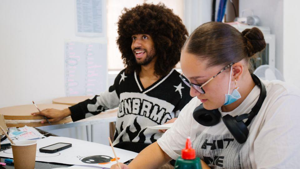 two young people - male (left), female (right) paint, laughing