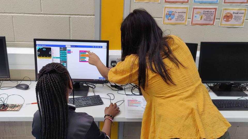 Female in yellow, standing, works with year 7 pupil, seated