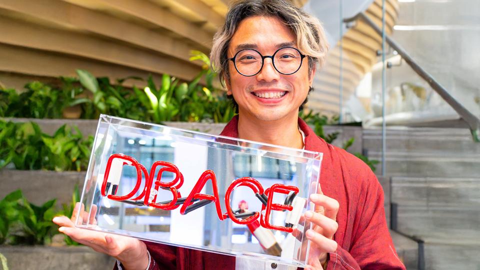 Kit, wearing a red jacket, holds a glass award with DBACE in red letters