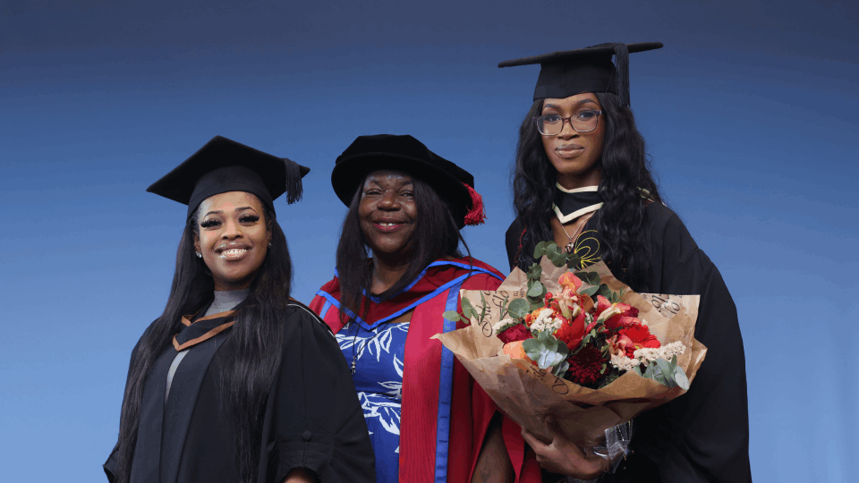 Two female undergraduates (l & r) pose with cappped female academic (centre) 