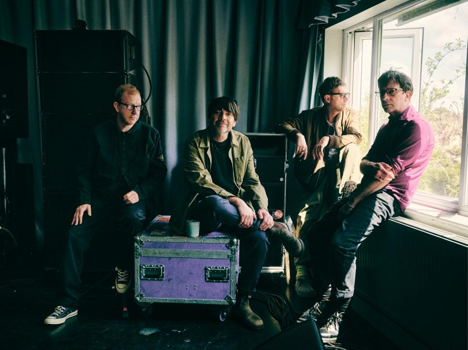 The members of the band Blur pose for a photo next to a window