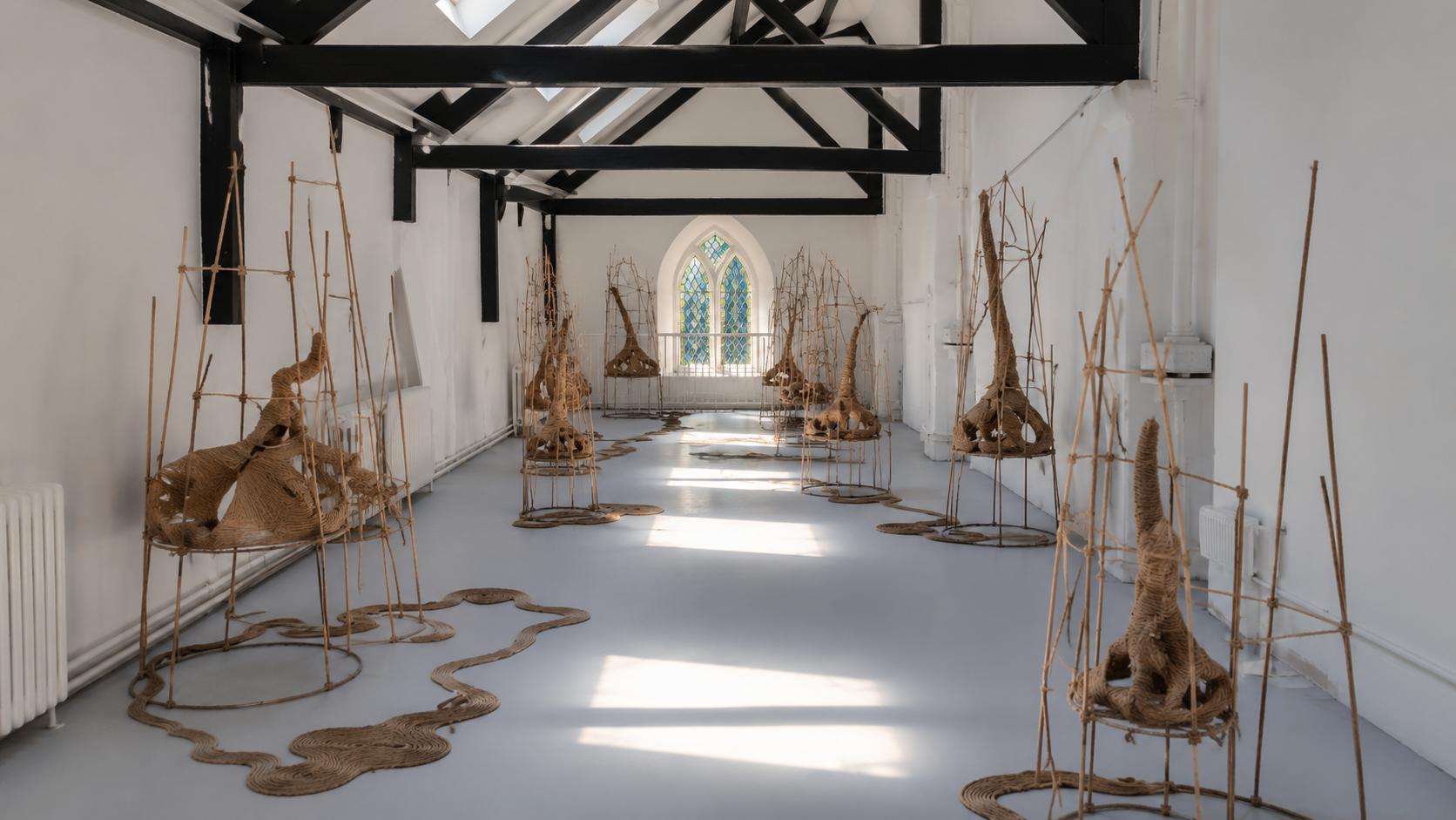 Rope structures in white gabled gallery, lit by sunlight through window at far wall. 