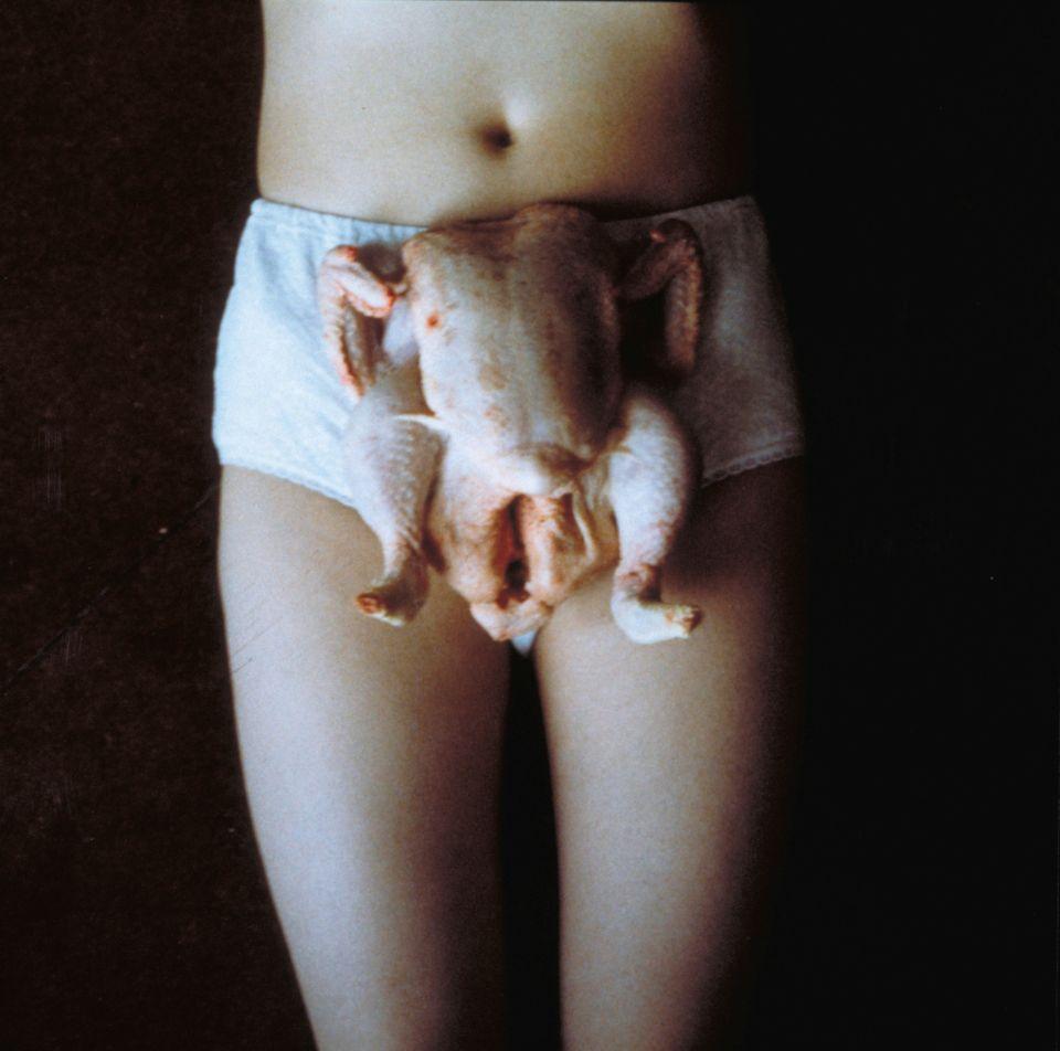 A photograph of a woman's lower torso and thighs wearing white knickers with a raw chicken placed on top.