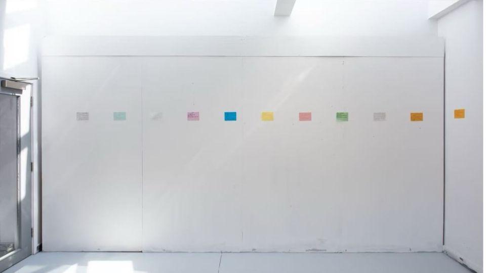 White gallery wall displaying a series of coloured text panels arranged in a horizontal line as part of Xinyi Miao's installation.