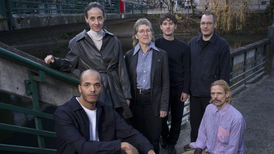 Four people standing and two people sitting for a group photo near some steps by a railing. 