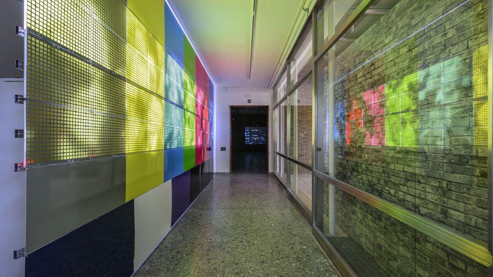 A corridor with colourful panels with light filtering through and casting colourful shadows