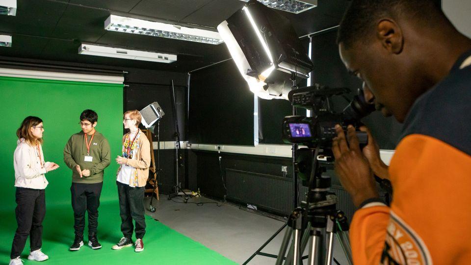 Three people stood in front of a green screen while another operates a camera