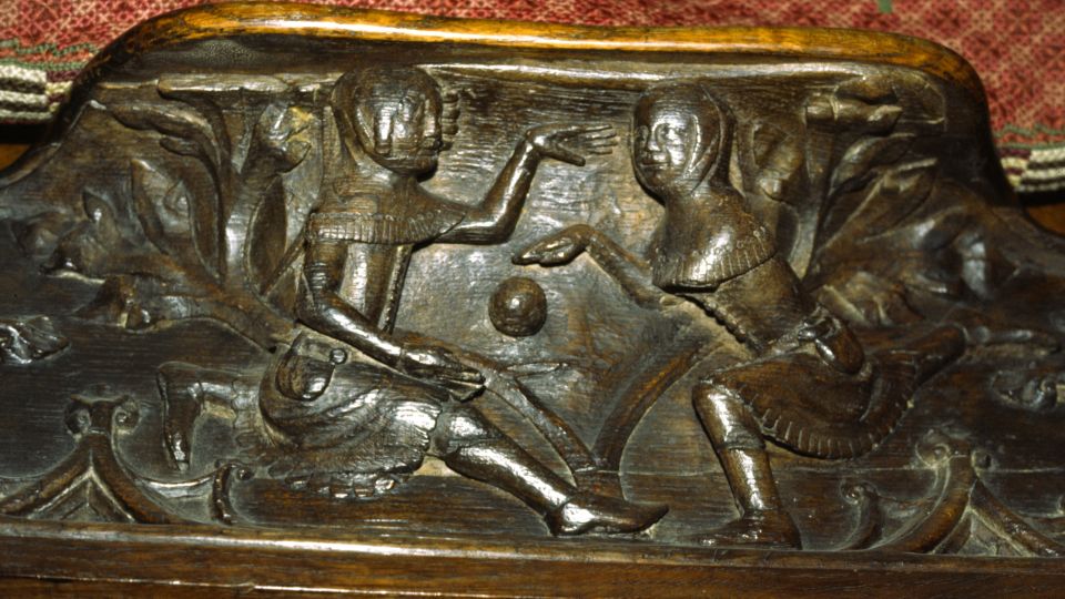 A wooden carving showing two figures in medieval clothing playing with a ball