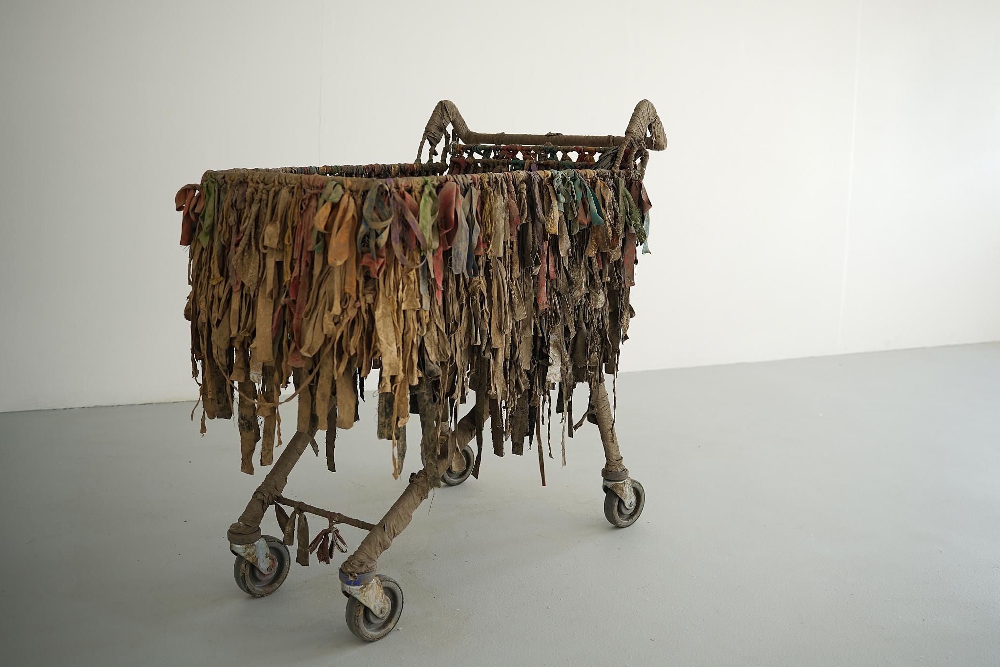Sculptural installation by Edith Marlowe Geenty featuring an aged shopping trolley draped with weathered ribbons.