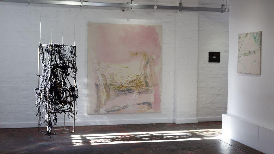 Some of the artwork on display including a large canvas on a white wall and a sculpture, casting a shadow onto the floor. 