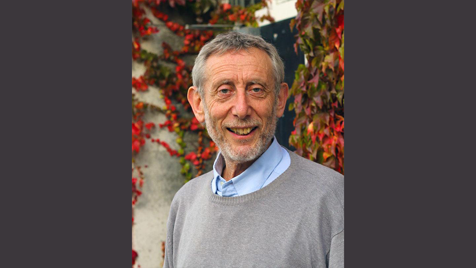 A portrait of Professor Michael Rosen wearing a grey jumper and standing in front of a background of ivy
