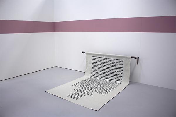 Artwork in a white room showcasing a scroll of text