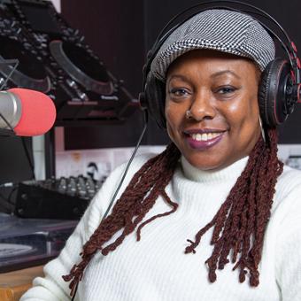 Graduate Kocoa, host of the Growing Through Goldsmiths podcast, wearing headphones while sitting at a desk in a radio recording studio.