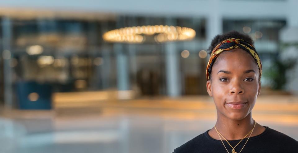 Zara, a Black woman, stands in a large corporate office space.