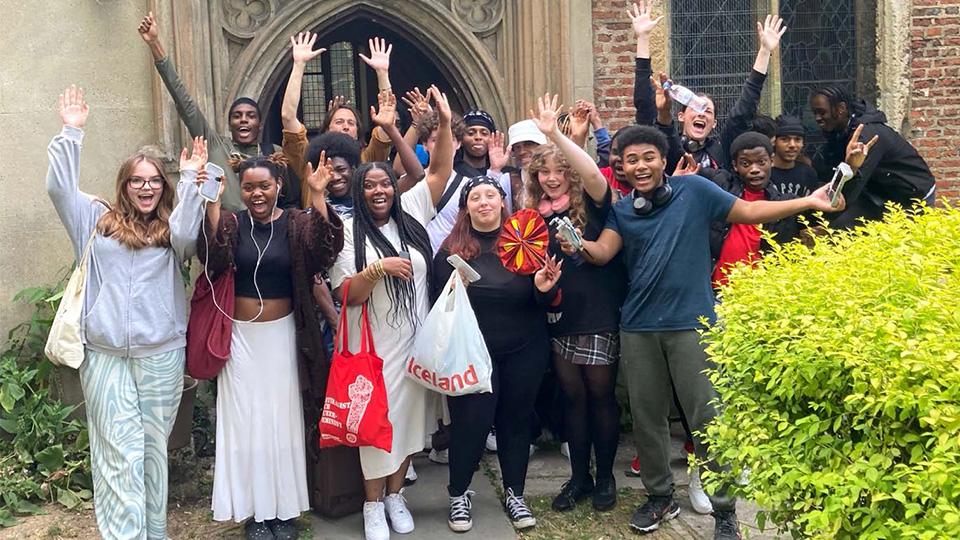 A group of young people pose outside a church in Stoke Newington with their hands raised in celebration.