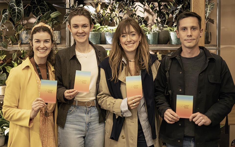 Four members of the Creativity Research Network looking at the camera smiling, holding Creativity Research Network leaflets