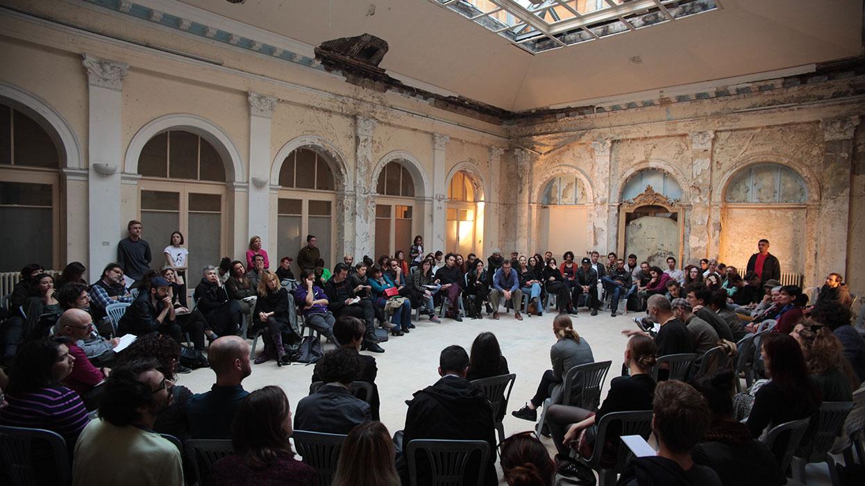 A group of people meeting in a large hallway in a circle.