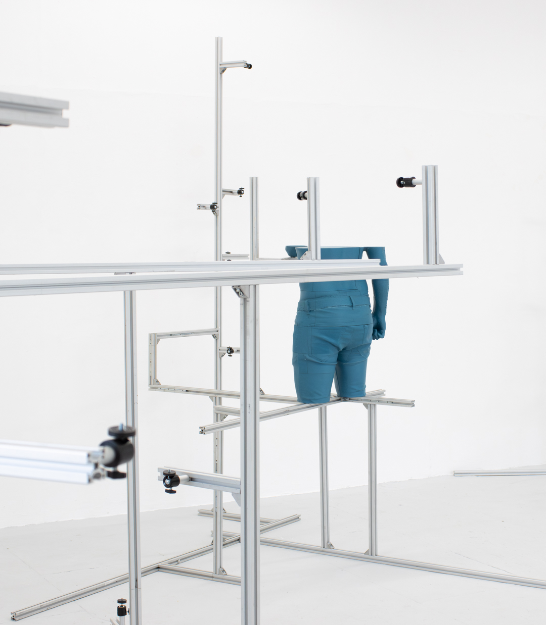 A blue 3D printed section of the human body wearing jeans from navel to upper thigh, held within a metal structure