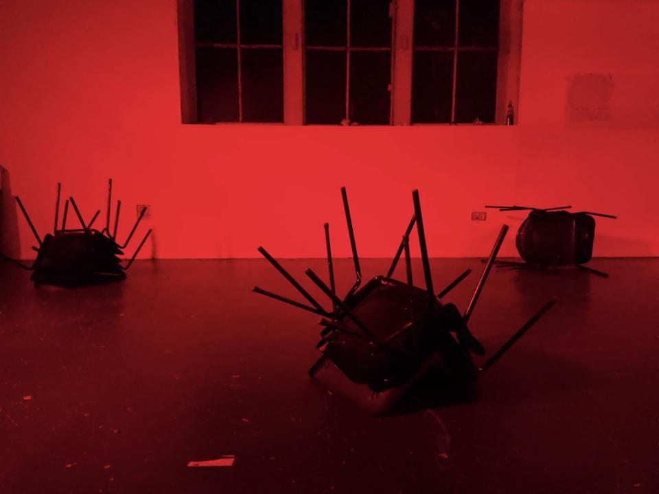 Three piles of chairs in a dark room only lit by a red light.