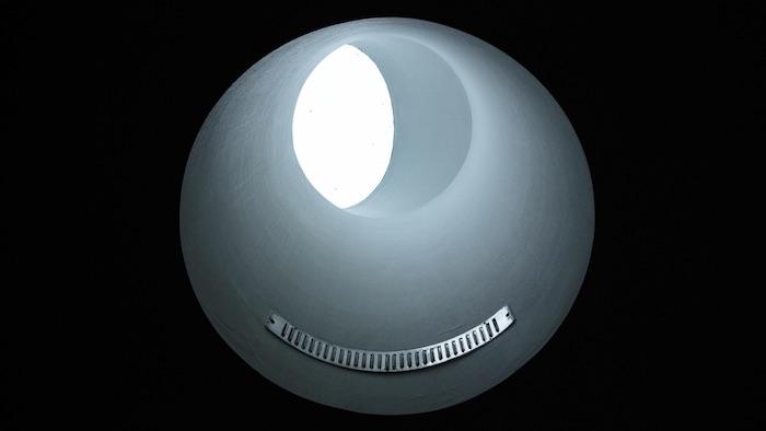 A blue sphere against a black background. At the bottom of the sphere sits a metal rail. At the top of the sphere is a white circle.