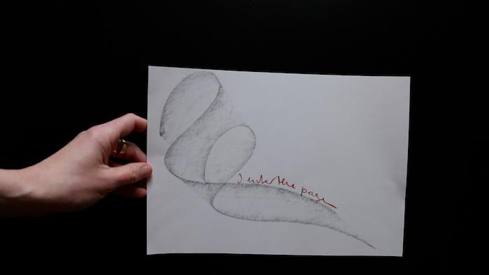 An image of a hand holding a drawing of an abstract line on a piece of white paper against a black background.