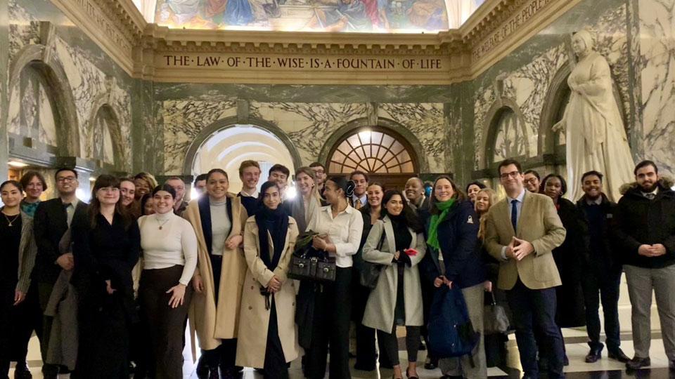 A large group of LLB Law with Criminal Justice & Human Rights students inside the Old Bailey, in an atrium that features the words 'the law of the wise is a foundation of life' along the wall