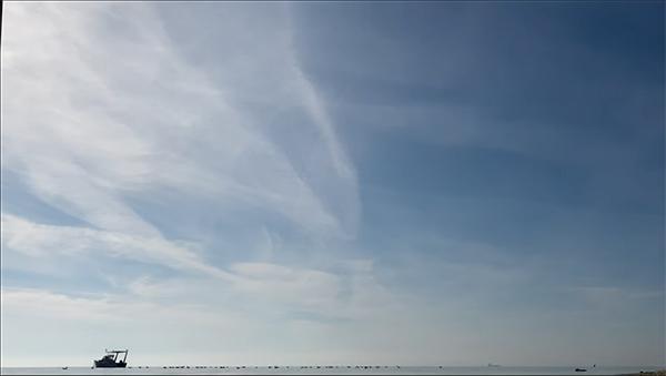 Video still of a horizon with a blue sky and white clouds and a boat in the distance.