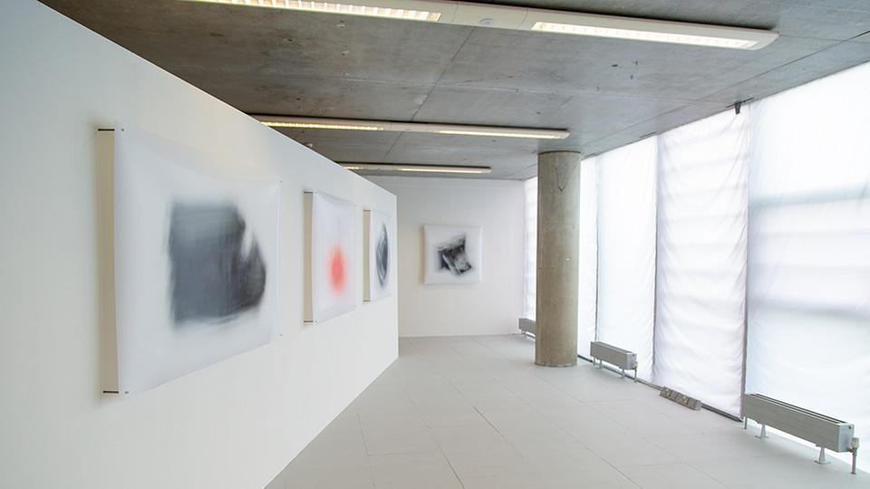 Muted colours are etched onto glass in a concrete exhibition space, with muffled light coming from windows