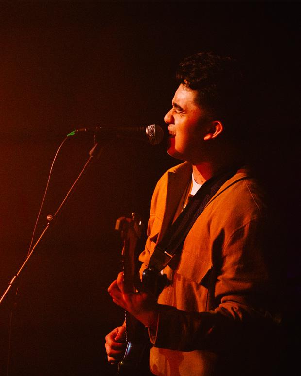 A man stands on stage singing with a guitar, the stage lighting is red