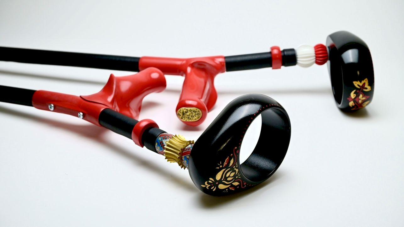 A red and black forearm crutch with gold patterns painted on
