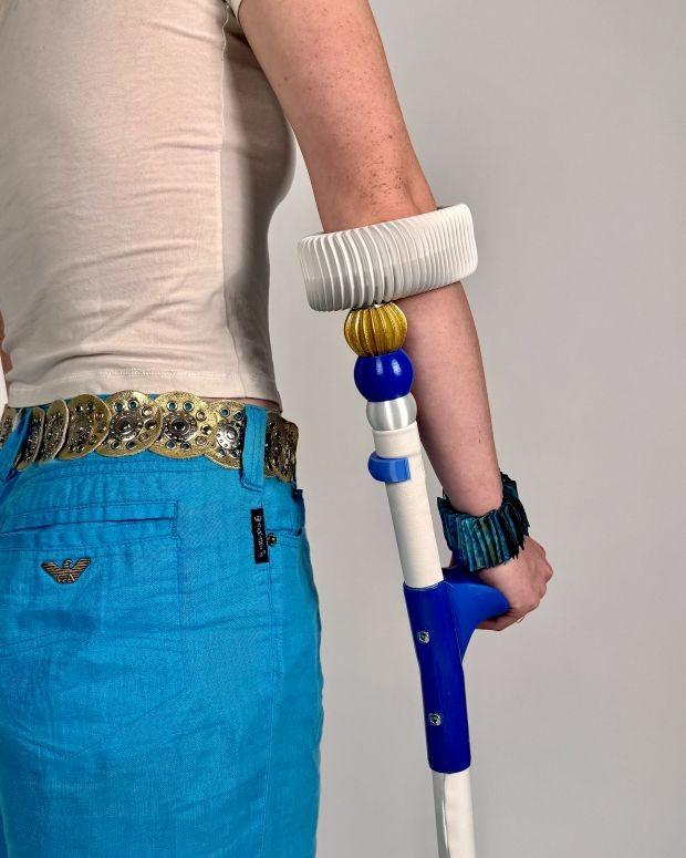 The back view of somebody using a blue and white forearm crutch with customisable beads