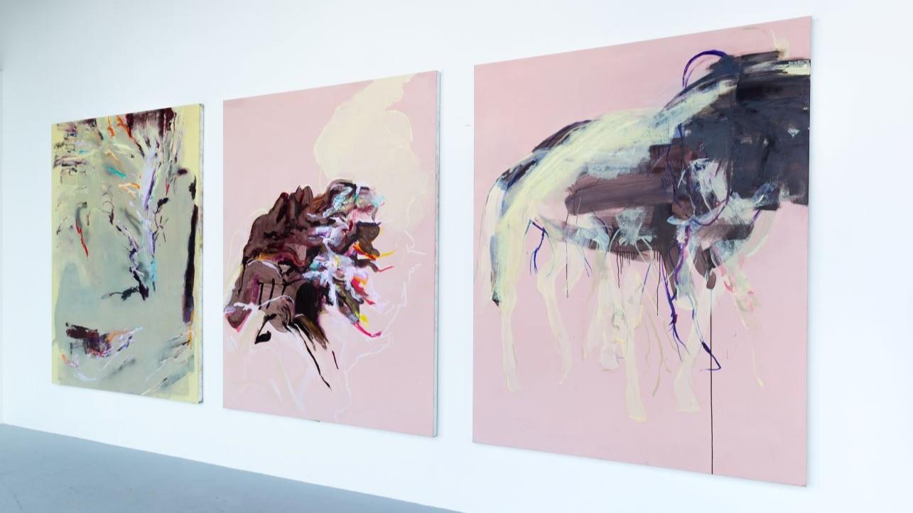 The same three canvases installed on a white wall shown from a side angle. 