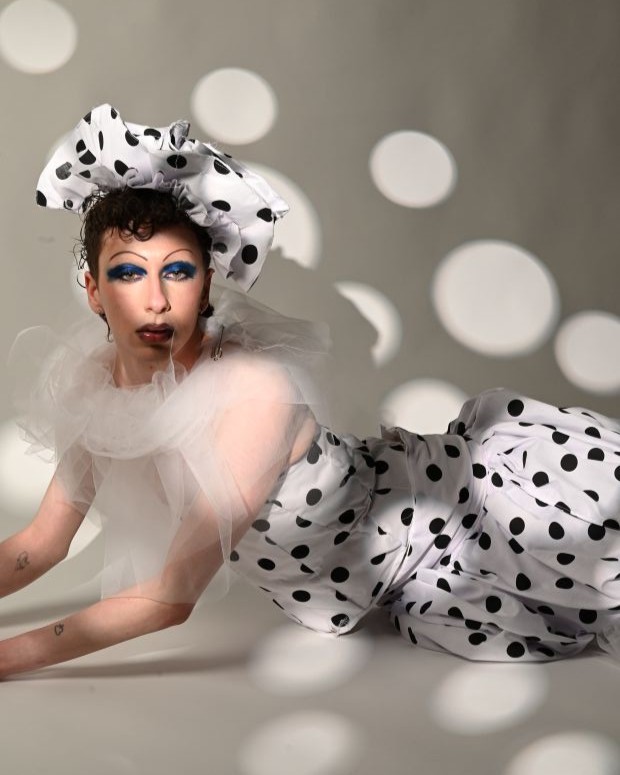 A model wearing clothes and a hat that are white with black polka dots with a collar made from netting 