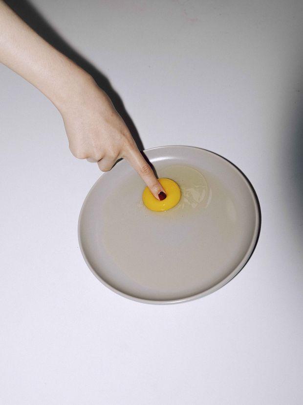 A raw egg on a grey plate, with a finger touching the yolk. 