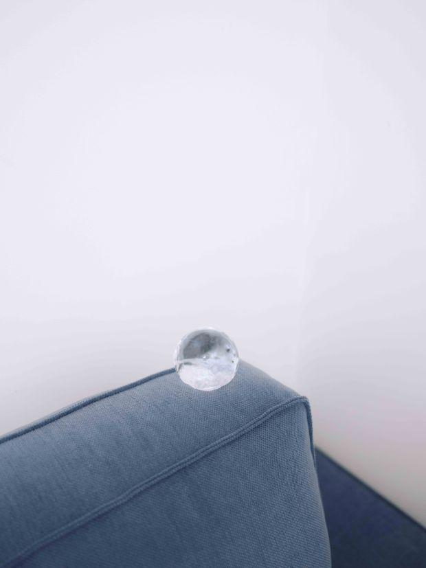 A photograph of clear sphere balanced on the back of a blue sofa 