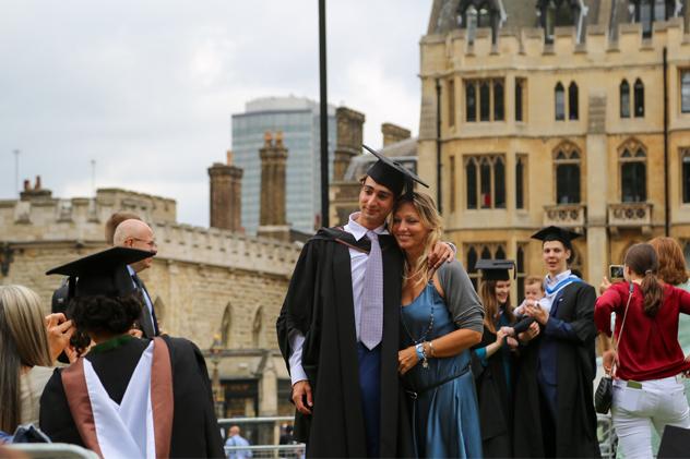 A student stands with a supporter and poses for a photograph before a graduation ceremony